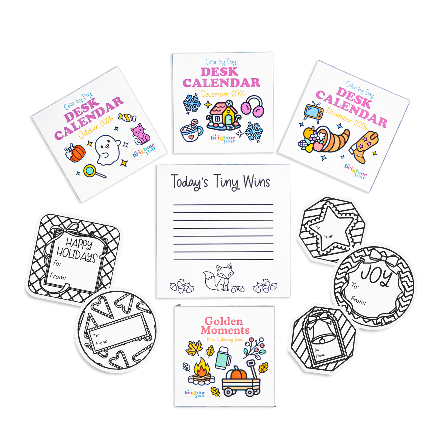 A variety of office accessories and stationery on a white background, including a 'Today's Tiny Wins' notepad, three A Brighter Year 'Color by Day Desk Calendar' mini coloring books, 5 colorable holiday themed gift tags, and a 'Golden Moments' Fall themed mini coloring book for adults.