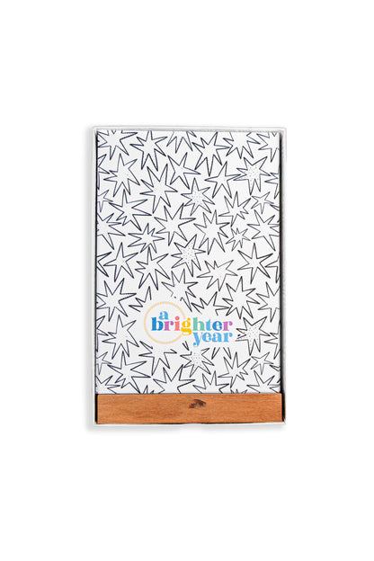 A color your own tarot deck in a box with a black starburst pattern and a colorful 'a Brighter year' logo near the bottom. It has a natural wood slide cover and is photographed on a clean white background.