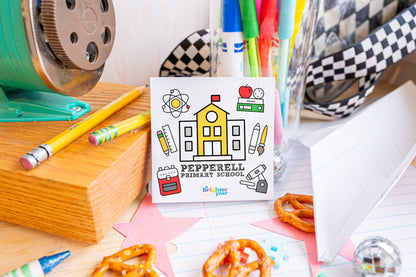 Pepperell Primary School mini coloring book with a yellow school-house cover, surrounded by pencils, markers and school supplies